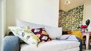 Un salón moderno con un sofá gris, cojines estampados, una mesita con un florero y un panel decorativo en la pared.