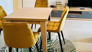 Una sala de estar moderna con una mesa de comedor de madera, sillas amarillas, un televisor de pantalla plana y una lámpara colgante decorativa.