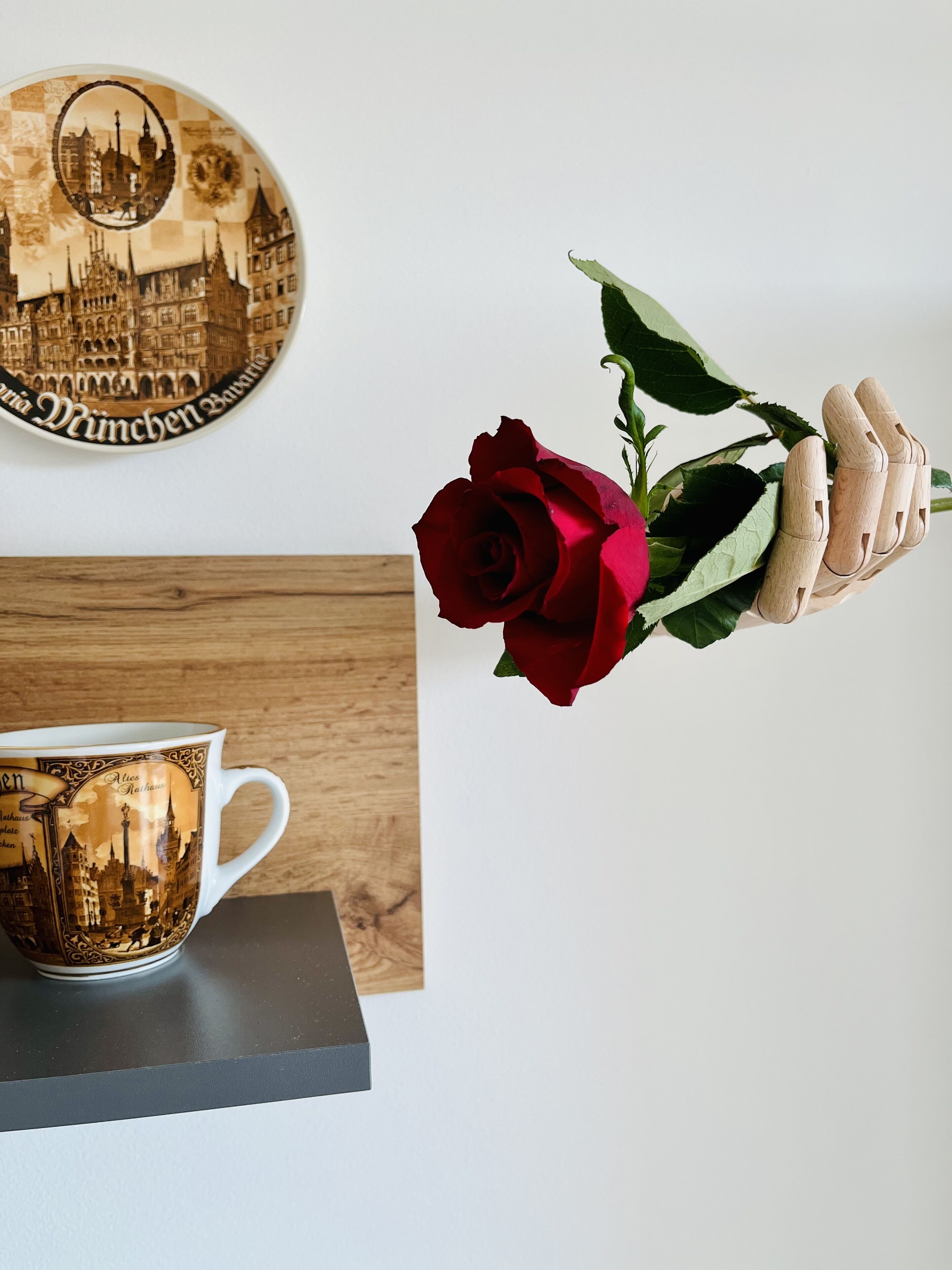 A wooden mug with a cityscape design, a red rose, and a wooden clothespin.