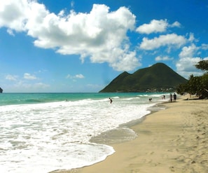 A beach with clear turquoise water, a sandy shore, and a mountain in the background.