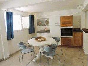 Una cocina compacta con armarios blancos, horno integrado y un comedor con mesa y sillas redondas.