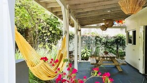 Un patio couvert doté d’un plafond en bois, d’un hamac, d’une table en bois sur laquelle est posée une plante en pot, et d’un luminaire suspendu en osier.
