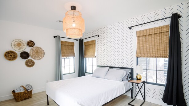 Un dormitorio moderno con una cama, una mesita de noche con lámpara y un ventanal con cortinas.