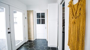 Un pasillo con suelo de baldosas hexagonales blanco y negro, puertas blancas y un tapiz de macramé amarillo en la pared.
