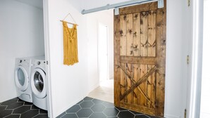 Un área de lavandería con lavadora, un tapiz de macramé y una puerta de madera estilo granero.