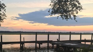 Une jetée en bois s’étendant au-dessus d’une étendue d’eau calme, avec un coucher de soleil en arrière-plan.