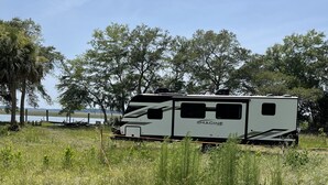 Un camping-car blanc de la marque « IMAGINE » est garé dans un champ herbeux, avec des arbres en arrière-plan.