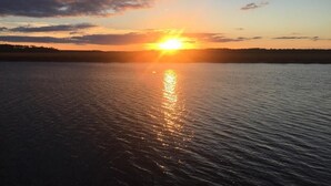 Un coucher de soleil sur une étendue d’eau calme, avec une côte lointaine à l’horizon.