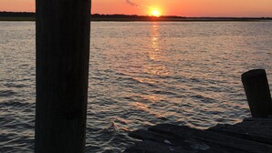 Une jetée en bois s’étendant sur une étendue d’eau calme, avec un coucher de soleil en arrière-plan.