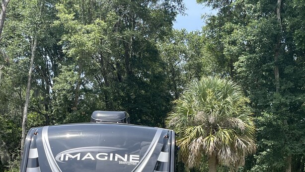 Un camping-car noir avec le mot « IMAGINE » écrit à l’arrière, garé dans une zone herbeuse, avec des arbres en arrière-plan.