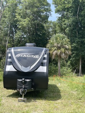 Un camping-car noir avec le mot « IMAGINE » écrit à l’arrière, garé dans une zone herbeuse, avec des arbres en arrière-plan.