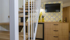 A staircase with wooden steps and white railings, leading to a room with a TV mounted on the wall and a patterned wallpaper. - Casa Di Camomilla (Platanias)