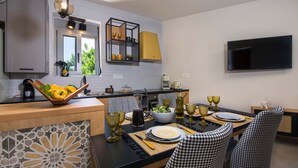 A modern kitchen with a dining area, featuring a black countertop, houndstooth chairs, and a flat-screen TV mounted on the wall. - Casa Di Camomilla (Platanias)