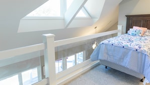 Een slaapkamer met een schuine kap, een bed met een bloemenbedekking en een witte leuning.