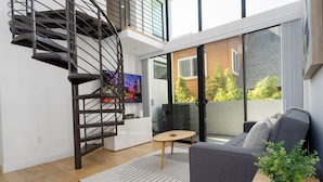 Un espace de vie moderne avec un escalier en colimaçon, un canapé gris, une petite table ronde et une plante en pot.