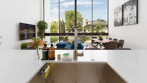 Une cuisine moderne dotée d’une grande fenêtre, un coin repas avec une table et des chaises, et un salon avec un canapé et une table basse.
