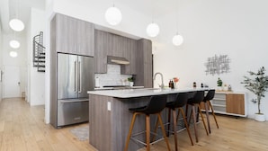 Une cuisine moderne dotée d’un îlot central, d’appareils électroménagers en acier inoxydable et de tabourets de bar noirs.