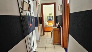 A hallway with a bed, a desk, and a television in the background. - Le gite à mamie (ORBEY)