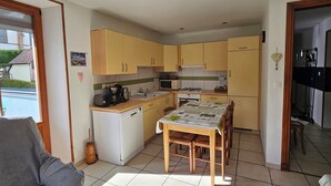 A compact kitchen with wooden cabinets, a dining table, and a built-in oven. - Le gite à mamie (ORBEY)
