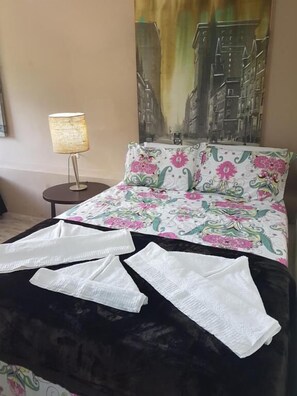 Un letto con una coperta a fiori, una lampada su un comodino e un dipinto con una veduta urbana sulla parete.