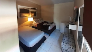 A compact hotel room with two beds, a bedside table with a lamp, a small desk, and a TV. - Pousada Maramar (Fernando de Noronha)