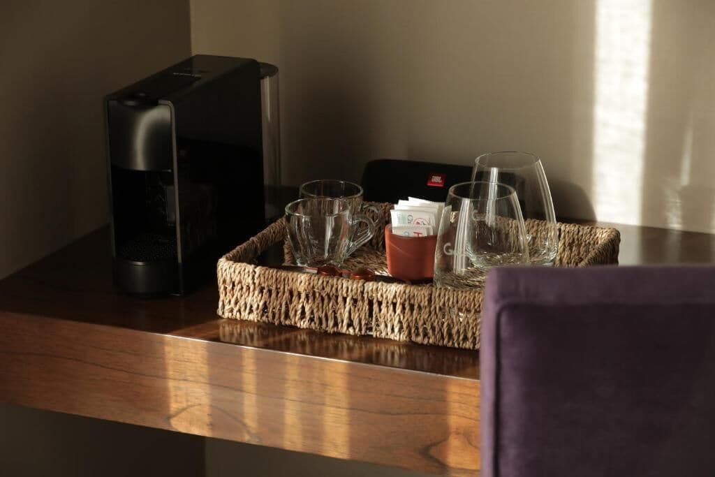 Uma cafeteira, um tabuleiro com chávenas e uma caneca, e uma caixa vermelha sobre uma mesa de madeira.