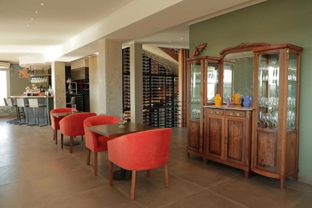 A dining area with a wooden table and red chairs, a wine rack, and a cabinet with glassware.
