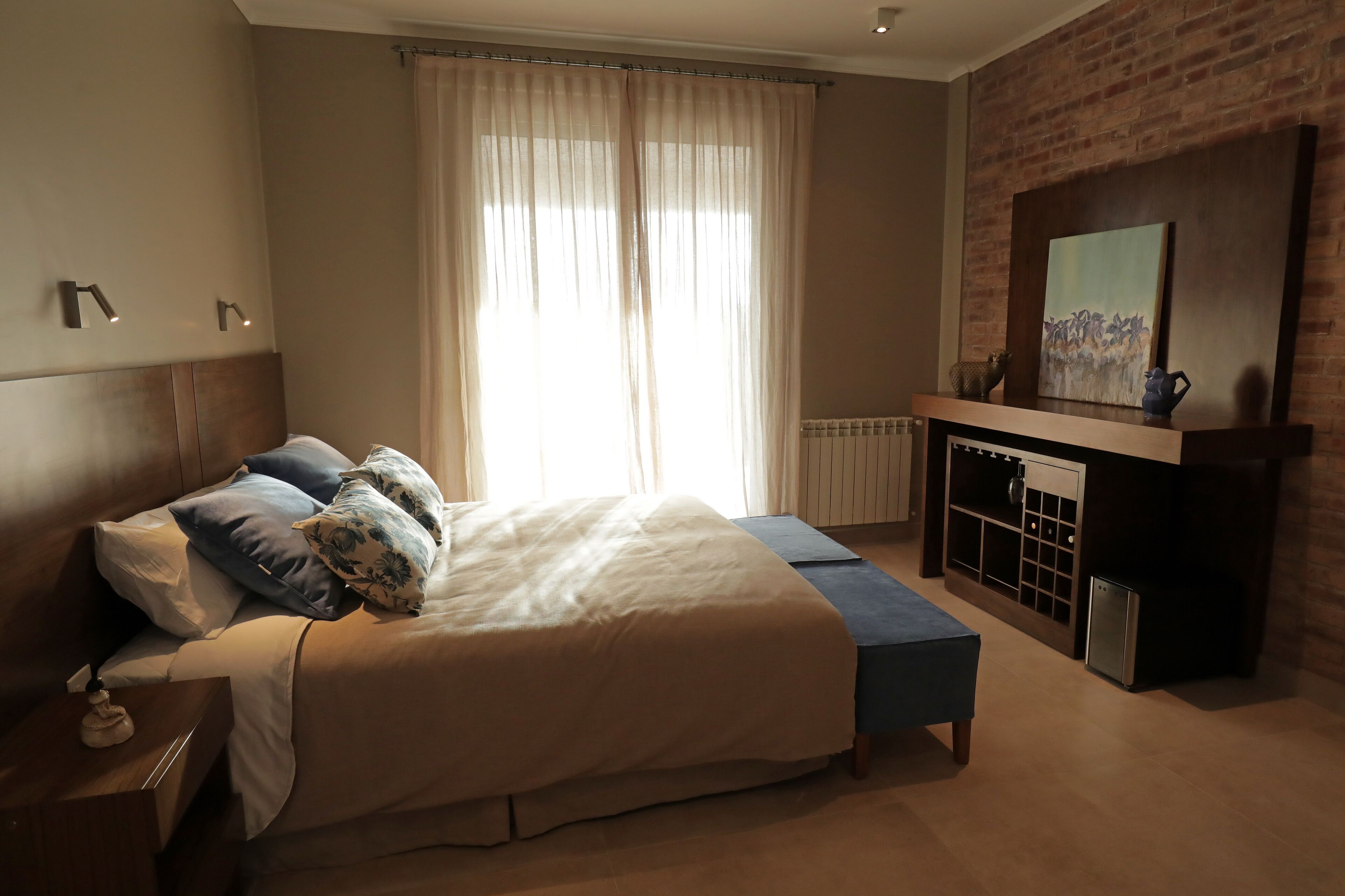 A bedroom with a large bed, a bench, a fireplace, and a painting on the wall.