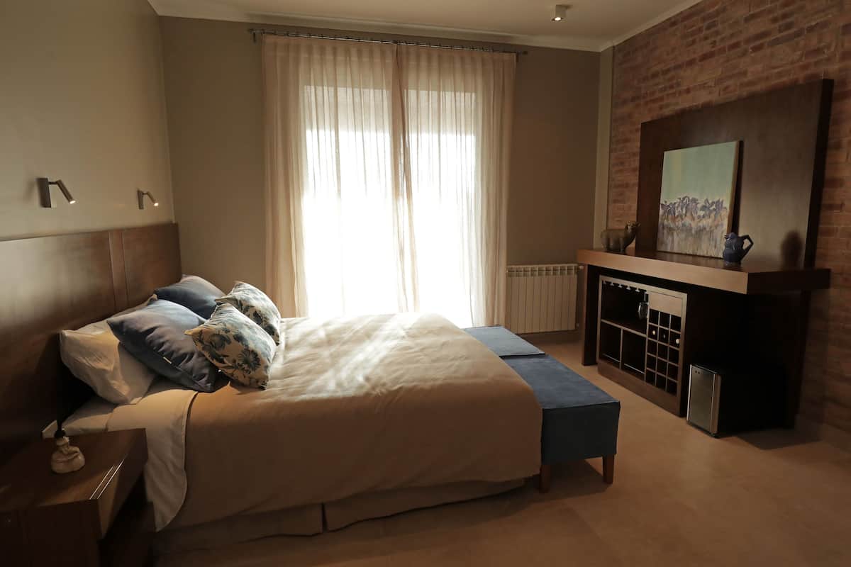 A bedroom with a large bed, a bench, a fireplace, and a painting on the wall.