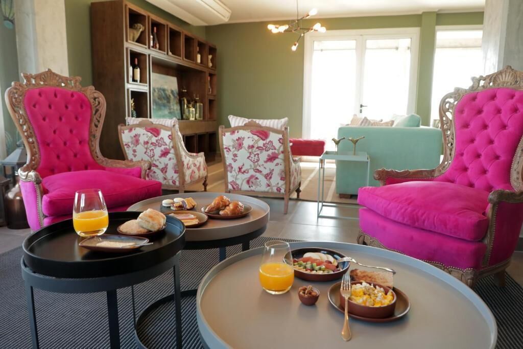 A living room with a bright green wall, a wooden bookshelf, and two round tables with breakfast items.