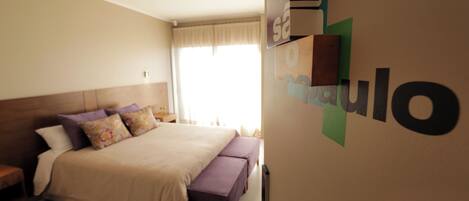 A bedroom with a bed, a bench, a nightstand, and a wall-mounted shelf.