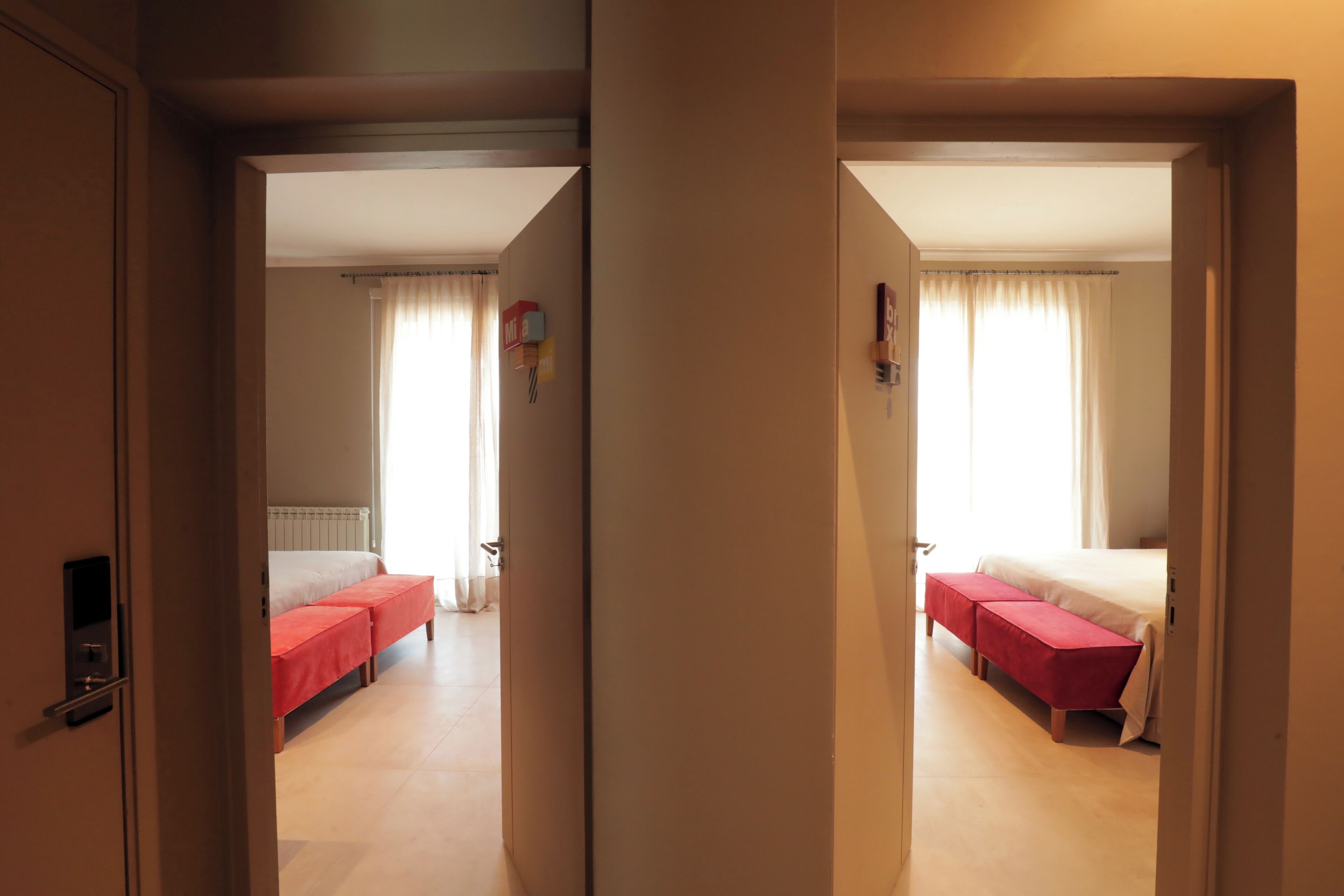 A hotel room with a bed, a bench, and a window with curtains.