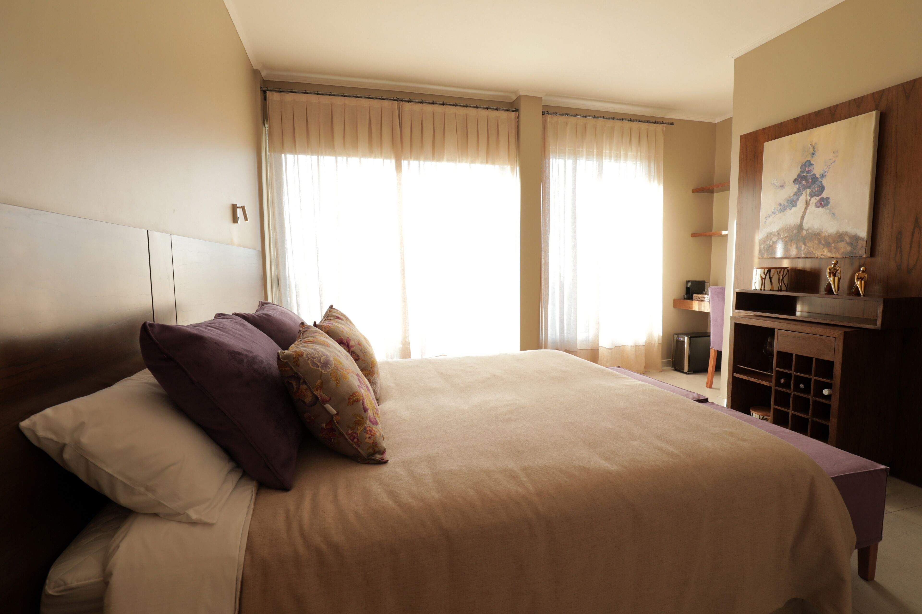 A hotel room with a large bed, a wooden headboard, a dresser with a mirror, and a painting on the wall.