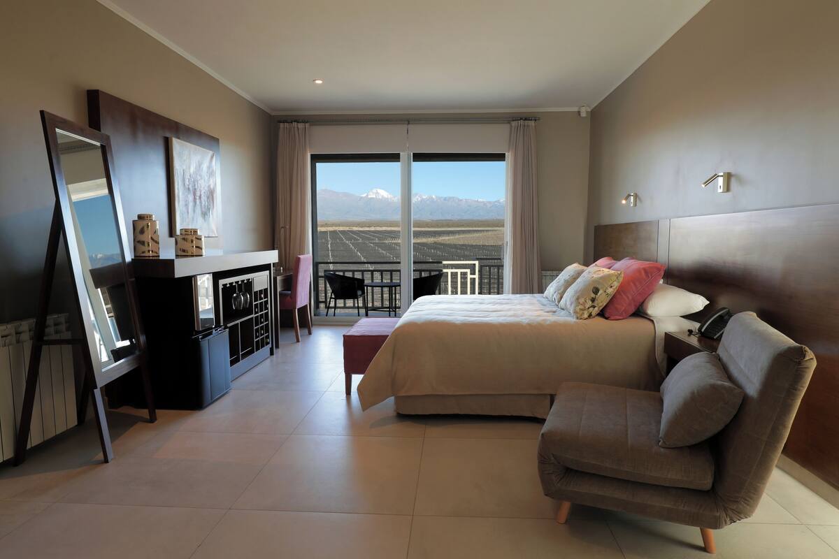 A modern hotel room with a large bed, a sofa, a desk, and a balcony with a mountain view.