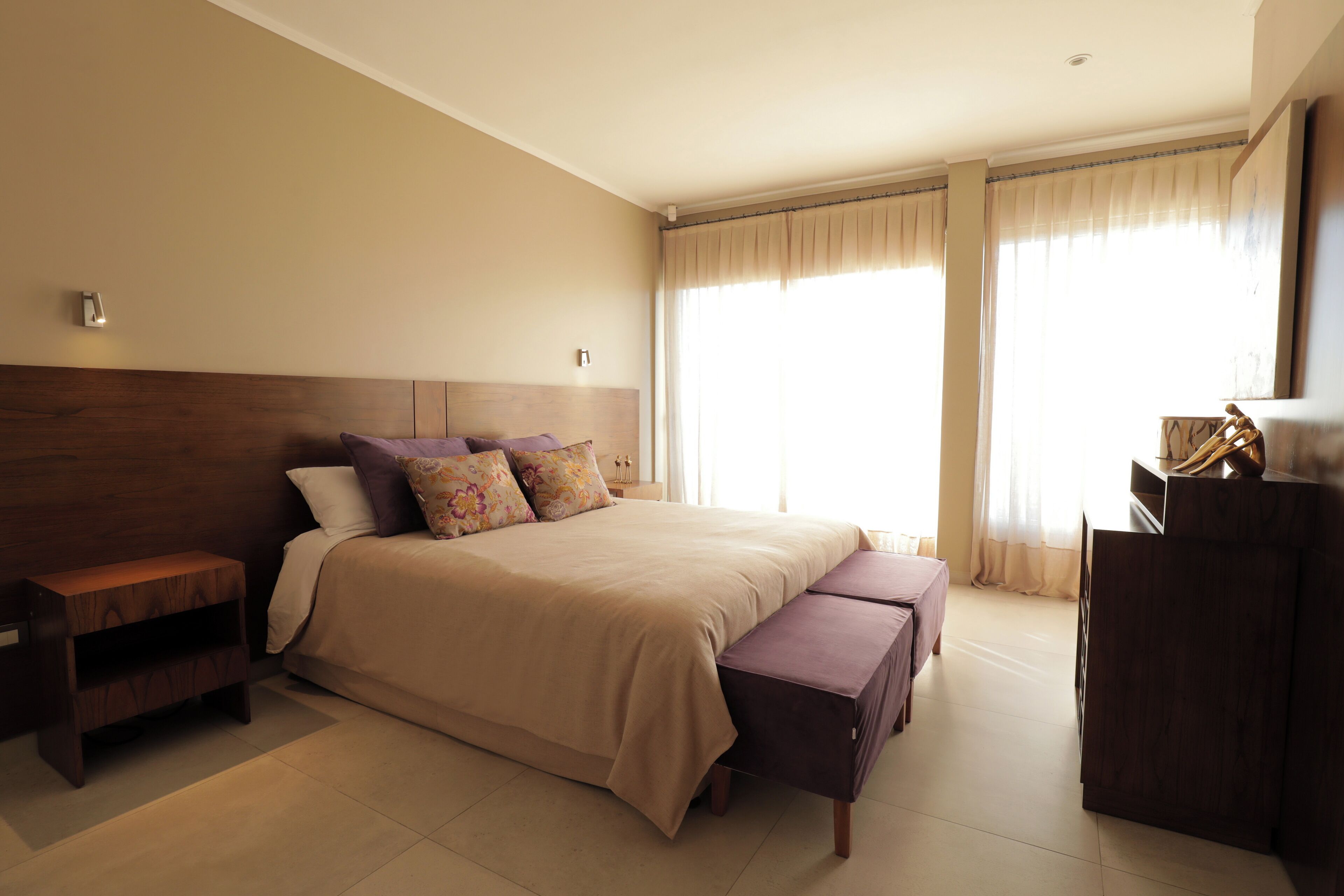 Un dormitorio con cama, mesita de noche, banco y cómoda.