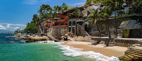 Un hotel frente al mar, con playa, palmeras y vistas al océano.