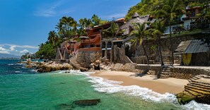 Un hôtel en bord de mer, doté d’une plage, de palmiers et offrant une vue sur l’océan.