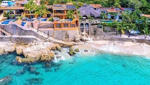 A coastal resort with multiple buildings, a rocky shoreline, and clear turquoise waters.