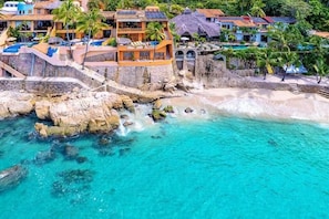 A coastal resort with multiple buildings, a rocky shoreline, and clear turquoise waters.
