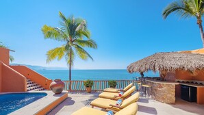 A poolside area with lounge chairs, a thatched-roof structure, and a view of the sea.