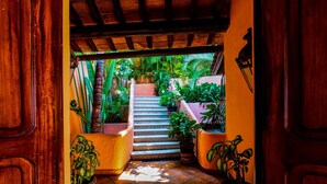 A wooden door opening to a staircase surrounded by potted plants, leading to a covered outdoor area with a tiled floor.
