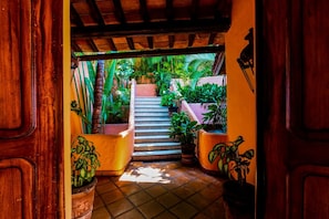 A wooden door opening to a staircase surrounded by potted plants, leading to a covered outdoor area with a tiled floor. - Villa Ventura 5 Star Luxury,Fully Staffed,Private Pool,Private Beach  (Puerto Vallarta)