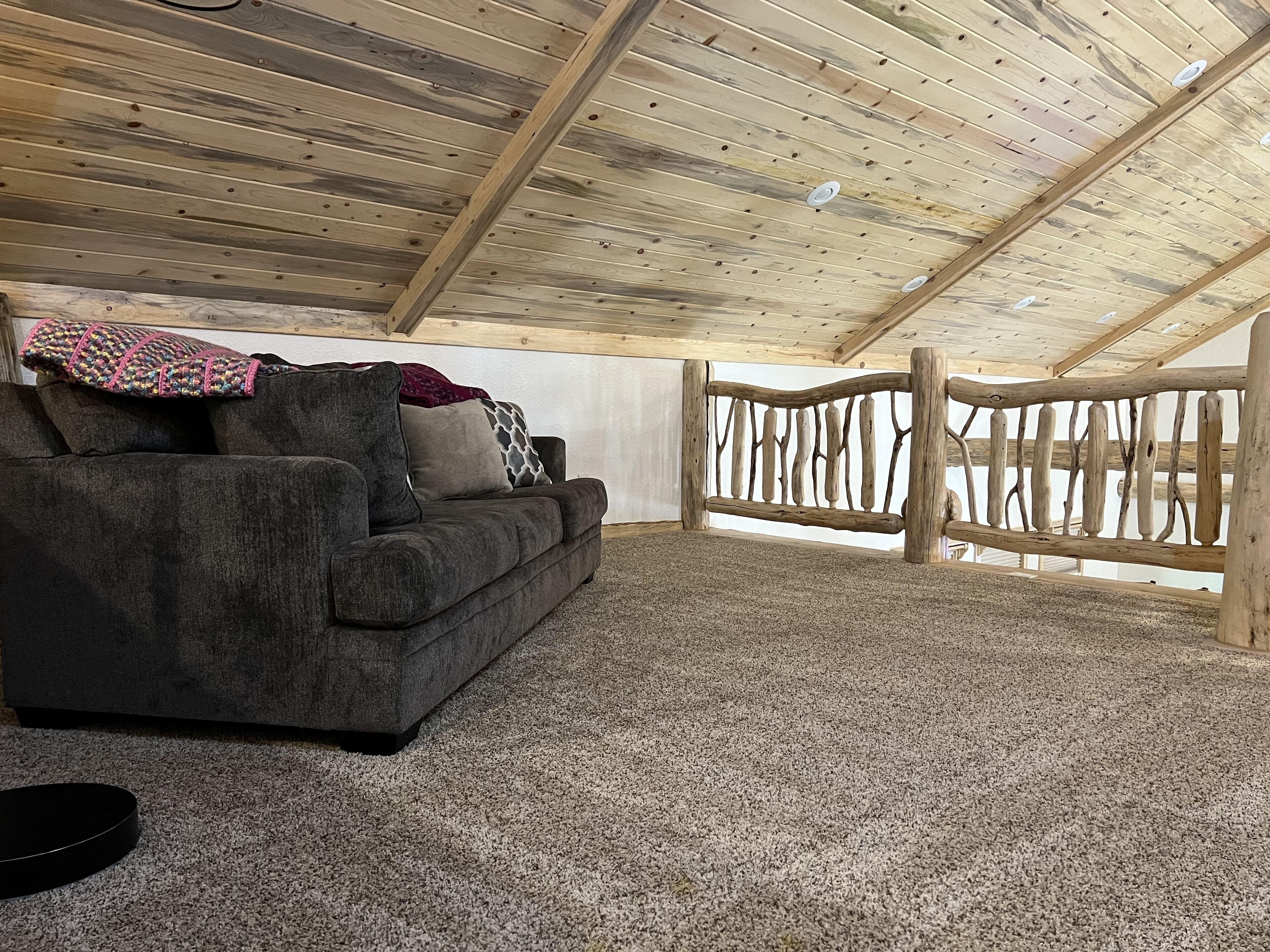 Ein gemütliches Zimmer mit grauem Sofa, Holzboden und einer rustikalen Holzreling.