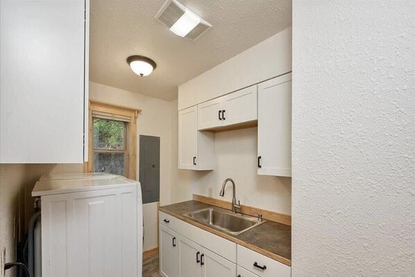 A compact kitchen with white cabinetry, a stainless steel sink, and a window. - Cutthroat Cabin: Large cabin with creek, 5 min. to Terrace Lakes for golf (Garden Valley)