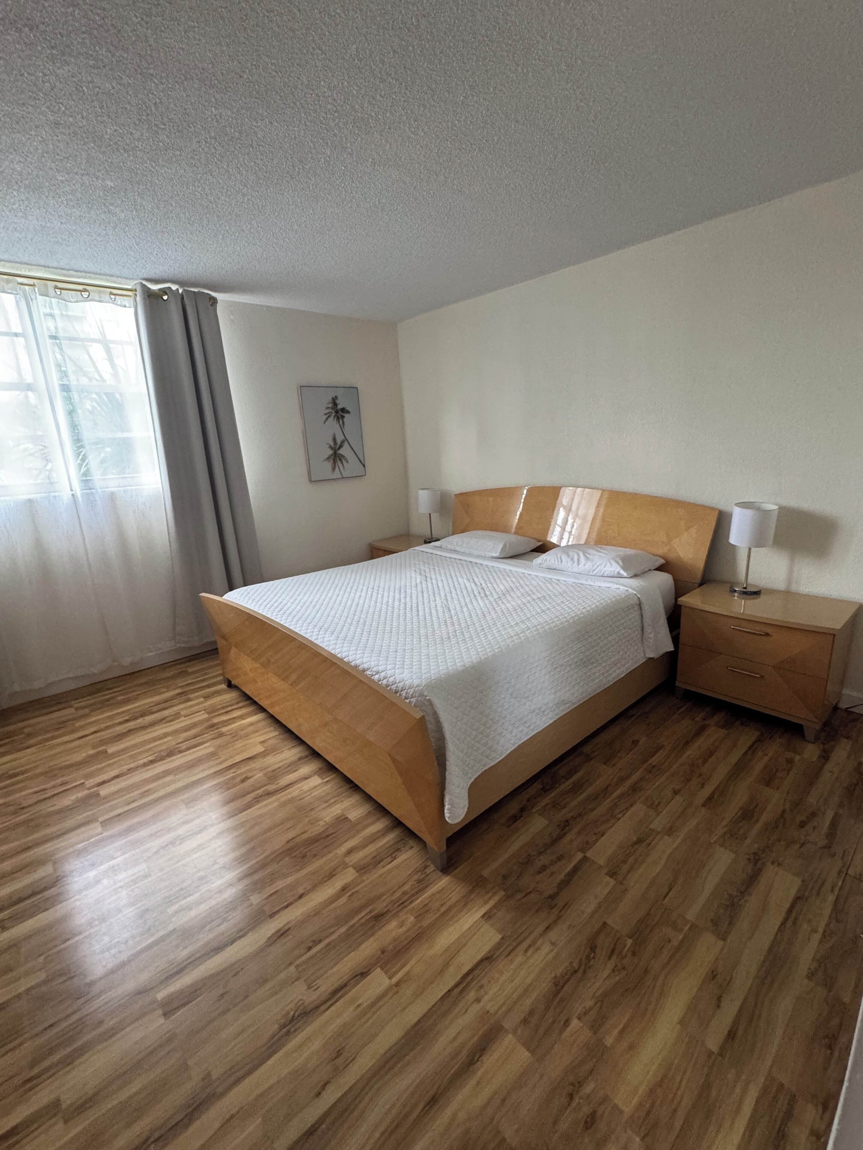 Un dormitorio con cama de madera, una mesita de noche, una lámpara y una ventana con cortinas.