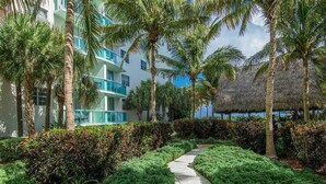A pathway flanked by lush greenery and palm trees, leading to a modern building with balconies. - Tropical ocean view one bedroom (Hollywood)