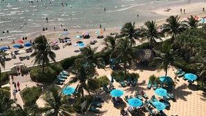 A beach with a pool, palm trees, and beach umbrellas. - Tropical ocean view one bedroom (Hollywood)