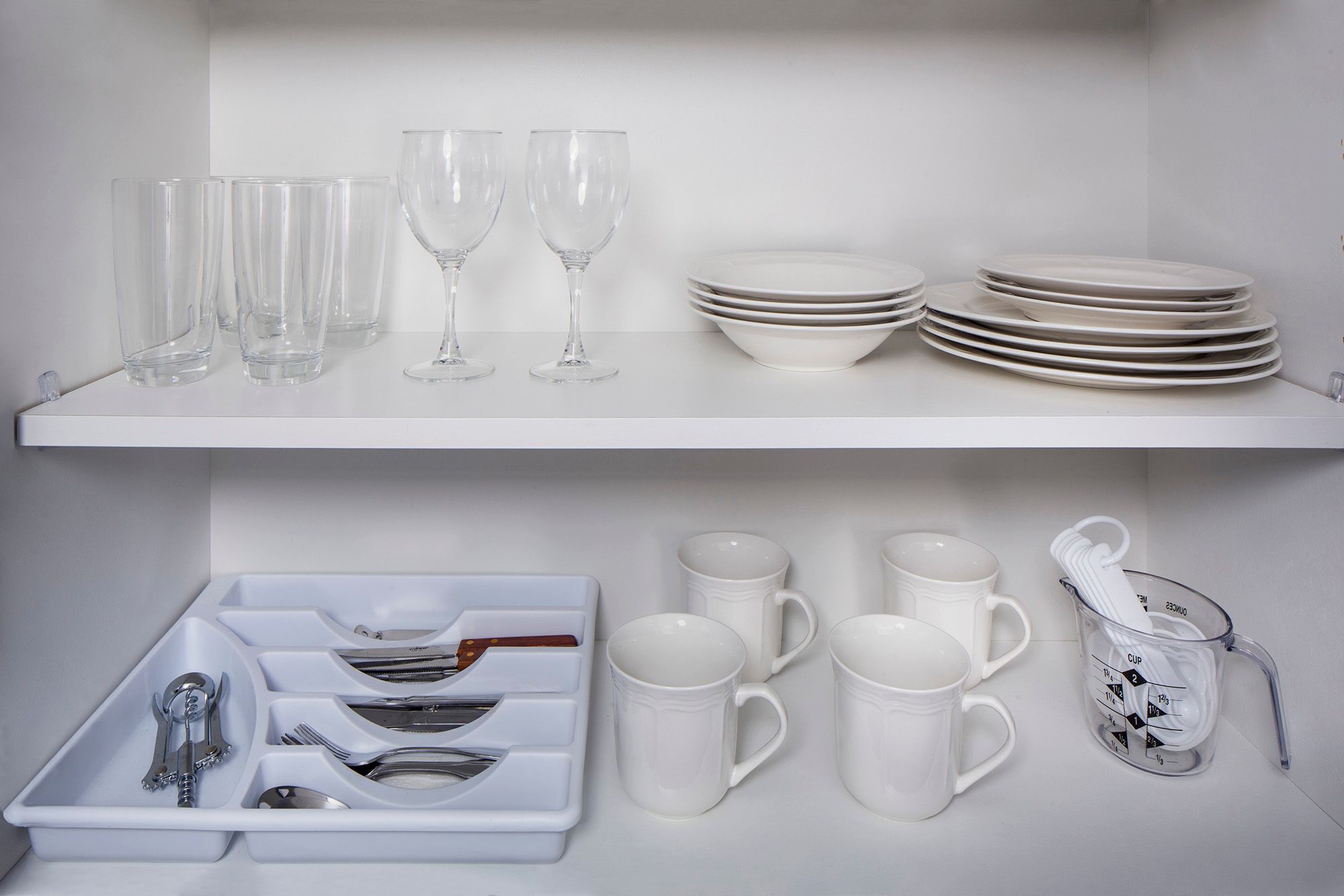 Una cocina con estantes blancos que exhiben vasos, platos y tazas.
