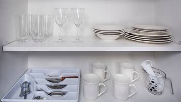 Una cocina con estantes blancos que exhiben vasos, platos y tazas.