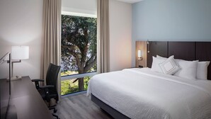 Habitació d'hotel amb un llit gran, una taula de nit, una cadira, una escriptori i una finestra que dona a arbres.